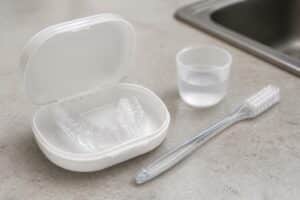 Clear night guard in an open case beside a toothbrush and rinse cup