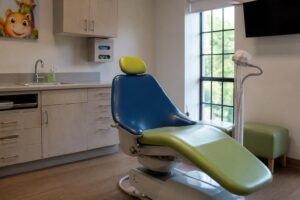 Empty pediatric dental exam room with a colorful child-friendly dental chair and a curing light on its stand